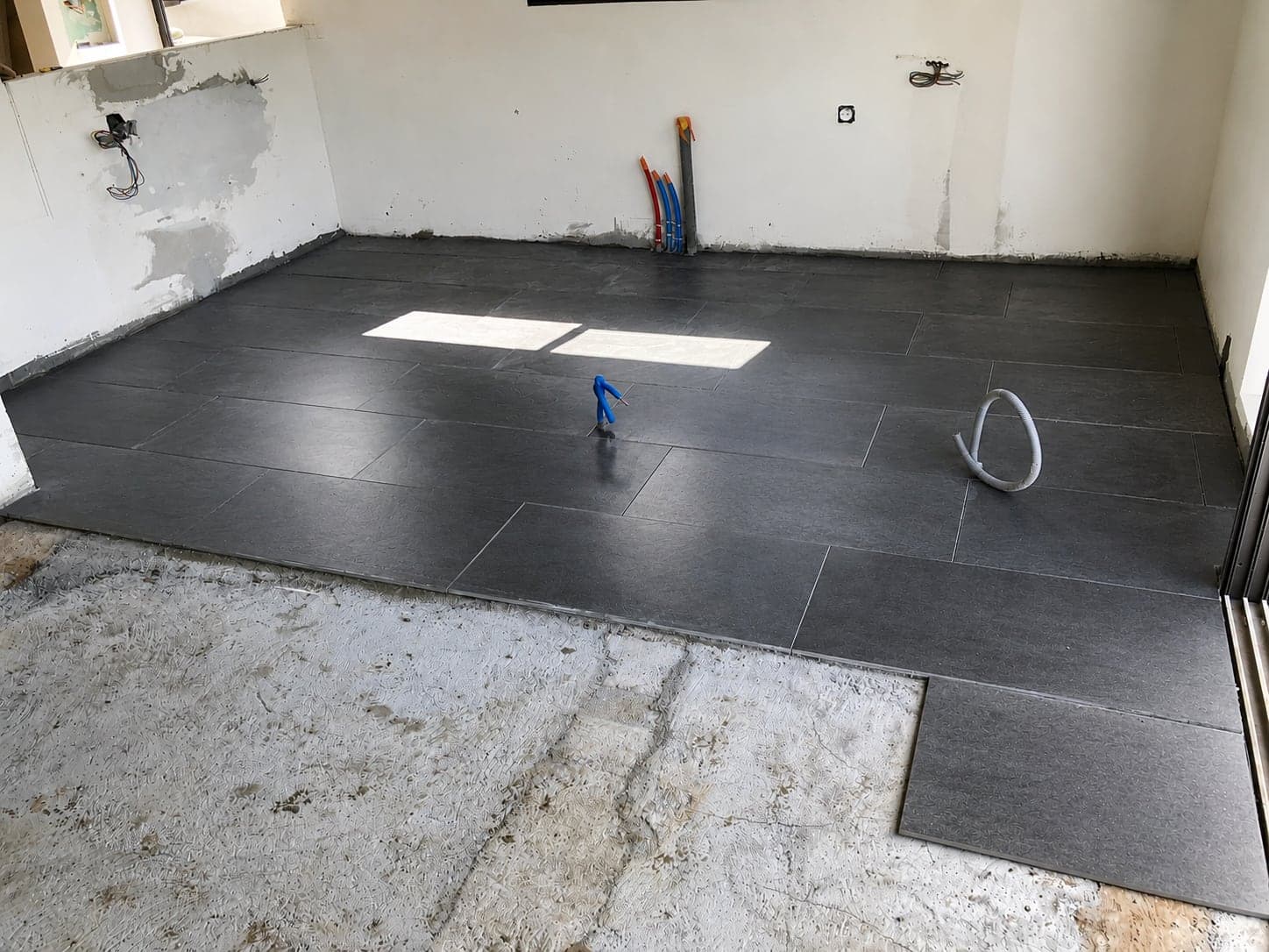 Pose du carrelage noir grand format sur la dalle, avant installation de la cuisine