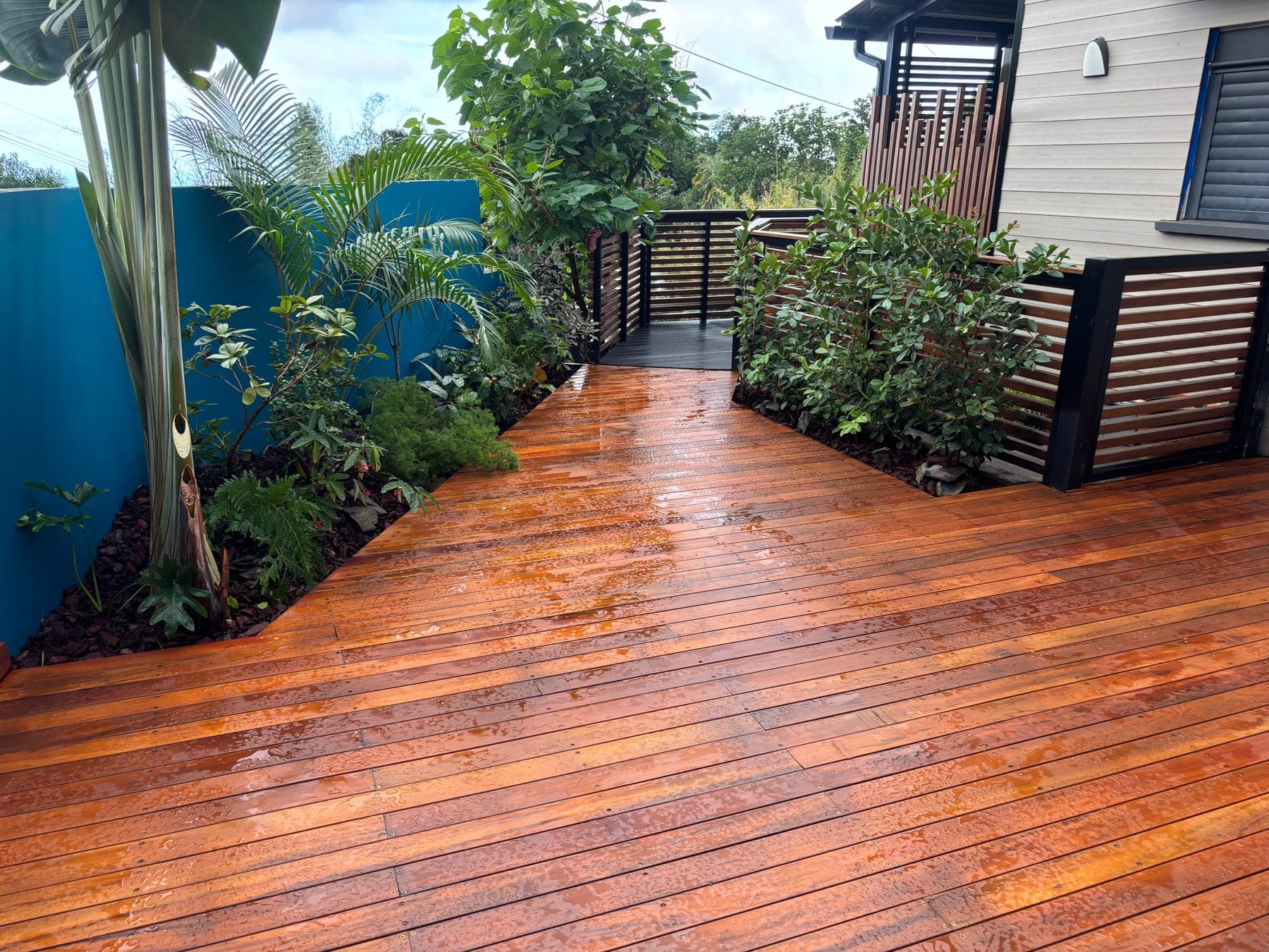 Terrasse en bois exotique bordée d'un massif de plantes tropicales, le long d'une maison à La Réunion