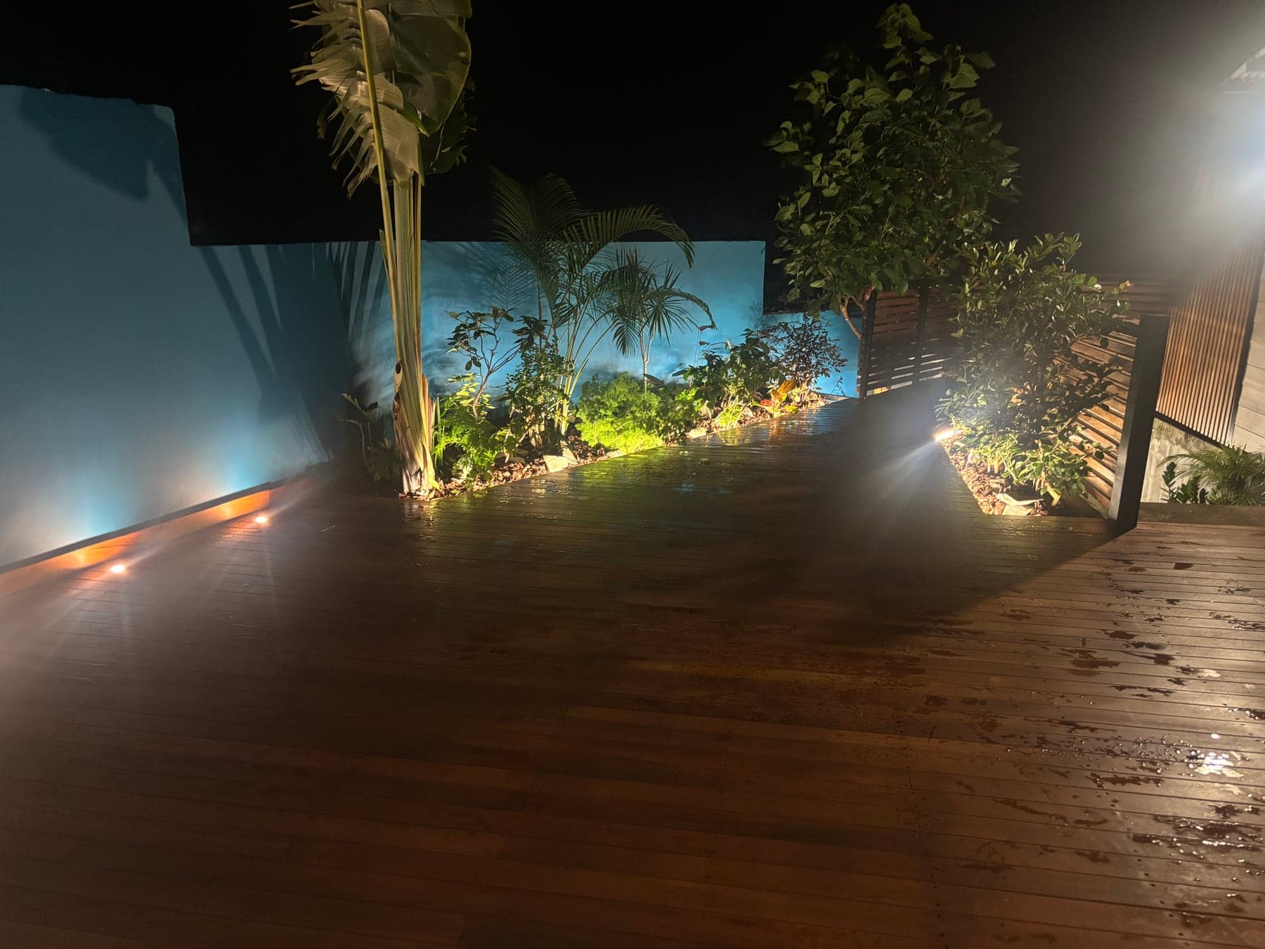 Terrasse en bois éclairée de nuit par des spots encastrés au pied du mur